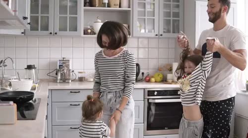 年轻的家庭和两个孩子在厨房跳舞，玩得很开心。