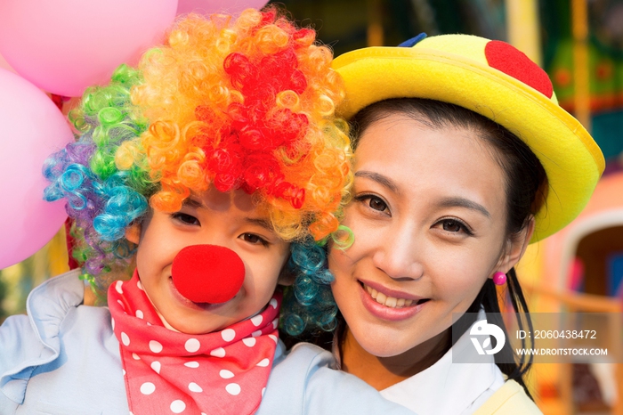年轻妈妈和扮成小丑的女儿在游乐园玩