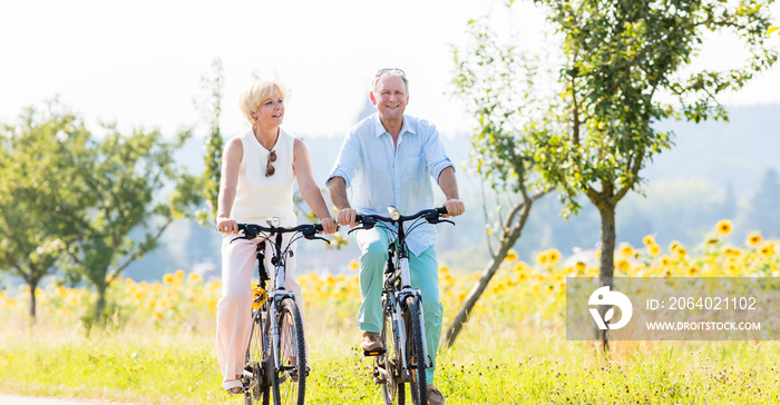 Senioren, Paar aus Frau und Mann, fährt Fahrrad an einem Sonnenblumen Feld