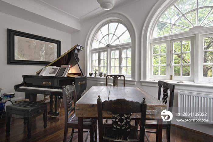 Chairs around wooden table with piano by arched French windows