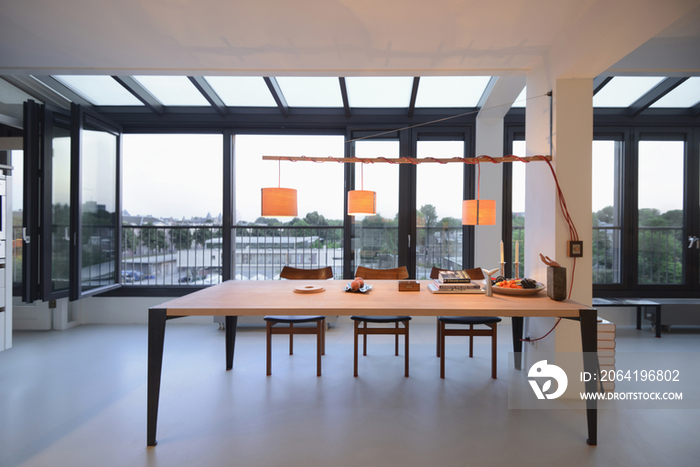 Lit lamps over dining table against large window in spacious and modern house