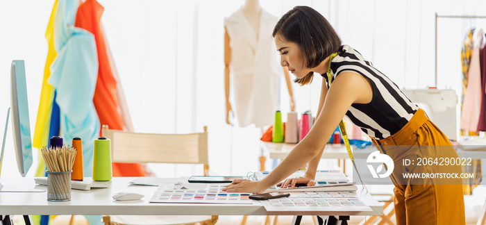 Young Asian designer woman working with computer and choosing multicolor chart at workplace, small b