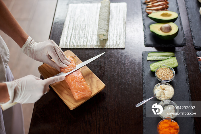 Close-up view of process of preparing delicious rolling sushi in restaurant. Female hands in disposa