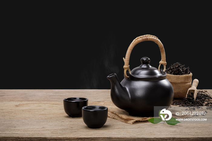 一杯热茶，配茶壶、绿茶叶和干香草，放在木桌上，隔绝黑背