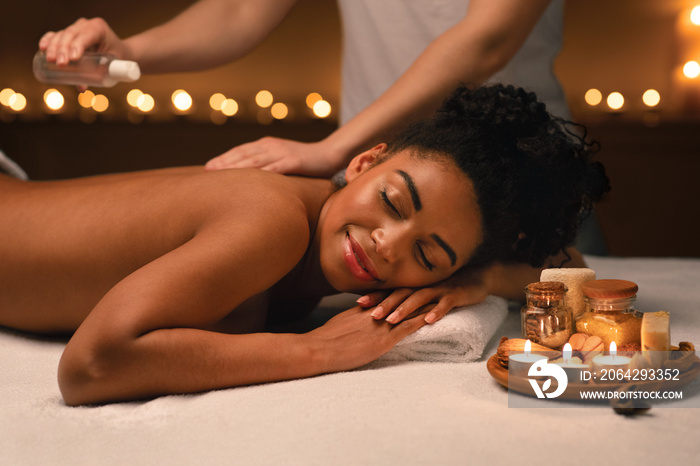 Therapist applying massage oil on beautiful black lady body