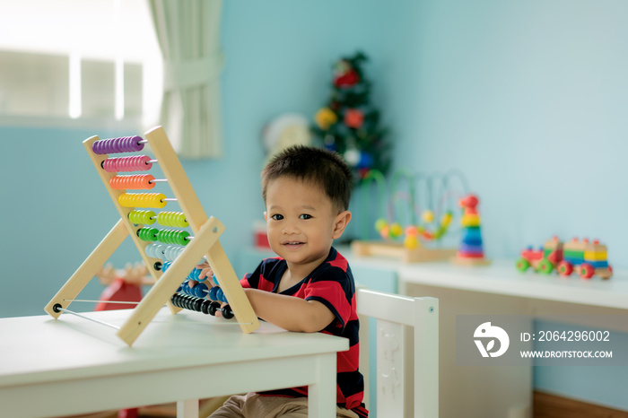 Asian Toddler baby boy learns to count. Cute child playing with abacus toy. Little boy having fun in