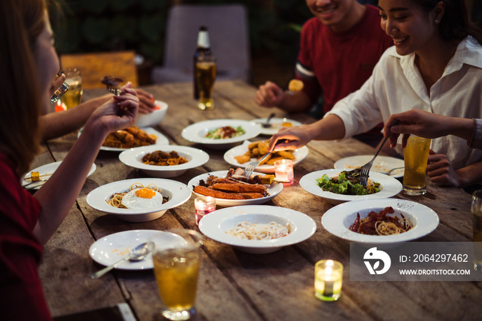 Asian group eating and drinking cold beer outside the house at night, having fun talking