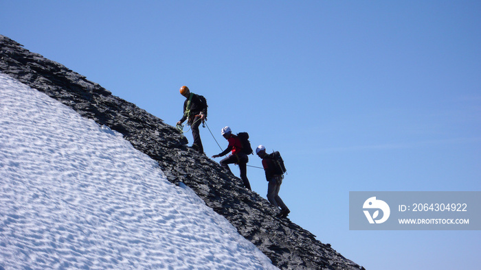 登山向导和两位客户前往一座高峰，在蓝天下登顶