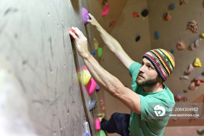 bouldern in einer Kletterhalle - junger Mann klettert eine künstliche Felswand empor // Bouldering i