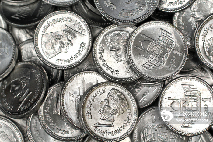 A close up image of a pile of silver Pakistani one rupee silver coins