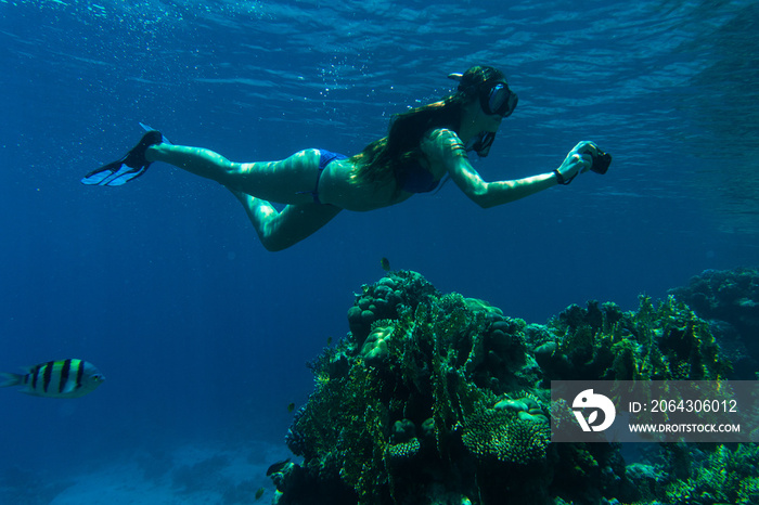 Young woman snorkeling with camera take photo over coral reef in blue sea