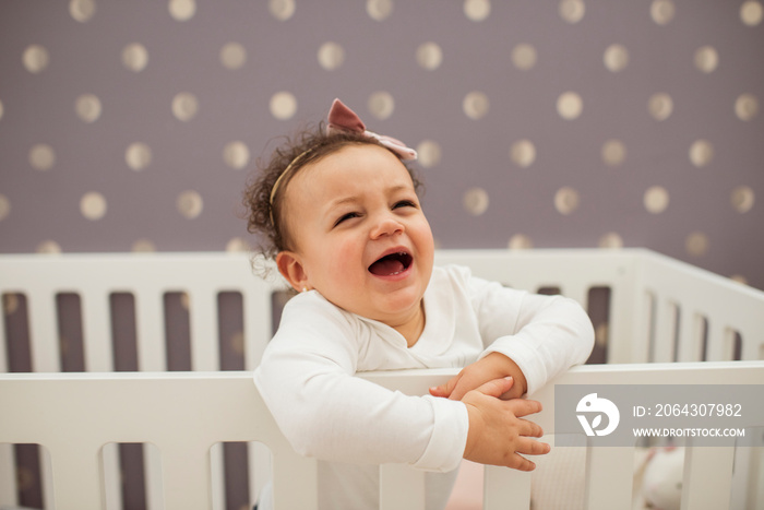 Close-up of cute baby girl crying while standing in crib against wall at home