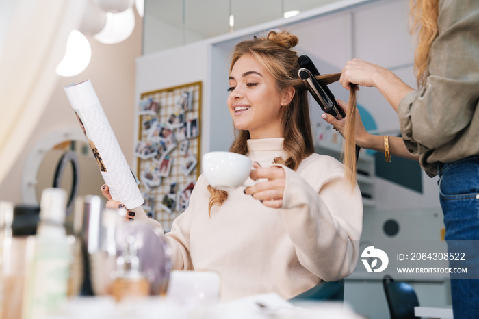 Blonde girl indoors in beauty salon with hairdresser.