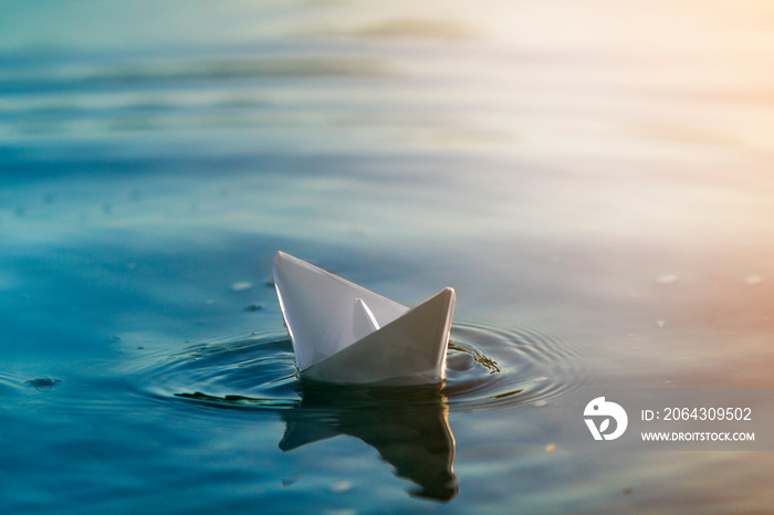 Close-up of simple small white origami paper boat floating quietly in blue clear river or sea water 