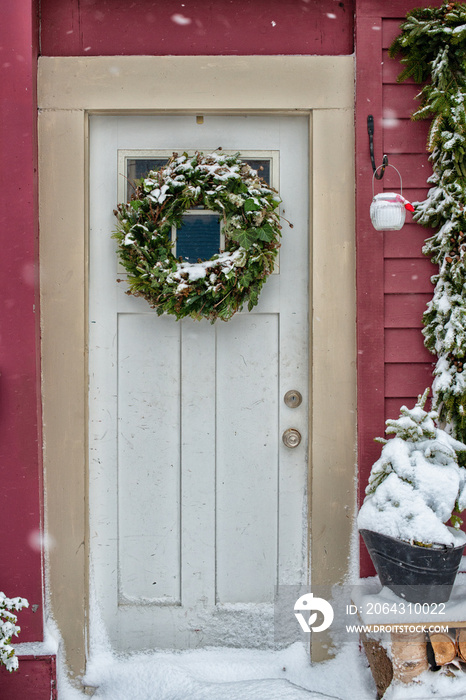 A solid white metal door with a cheerful Christmas wreath hanging on the window portion. The buildin