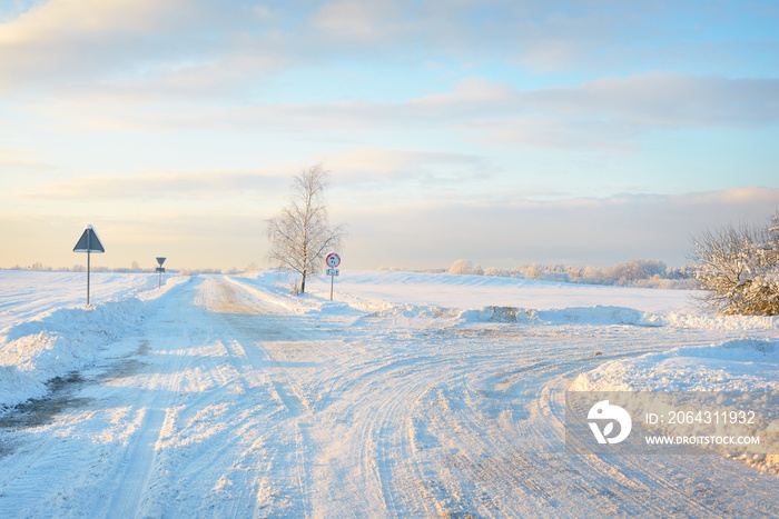 Country road through snow-covered field after a blizzard at sunset. Clear sky, golden light. Idyllic