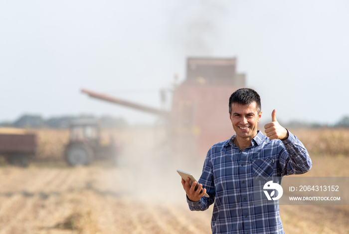 Farmer with tablet in front of combine harvester in soybean field