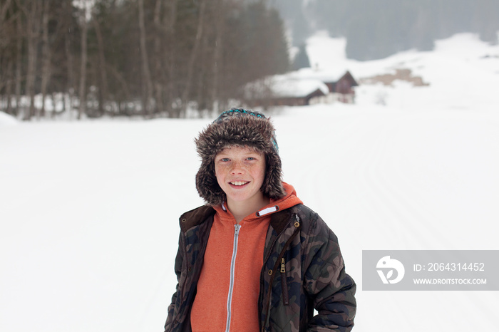 Portrait happy boy in fur hat in snowy field