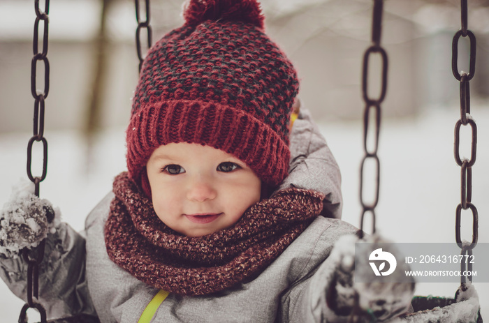 Funny little child girl wearing in red hat, a scarf, and a warm winter suit with gloves having fun a