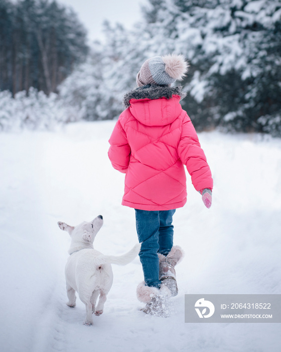 Little girl in a bright jacket plays in the winter snowy forest with her dog