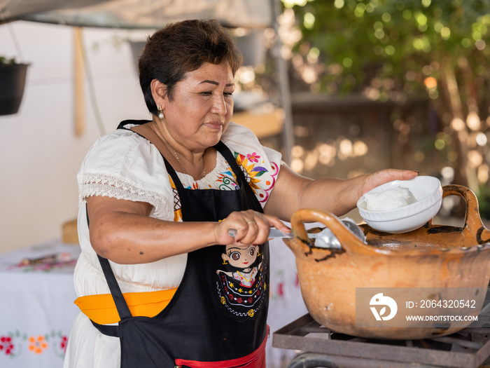 Horizontal, wide-view of an Indigenous woman cooking in an outdoor kitchen