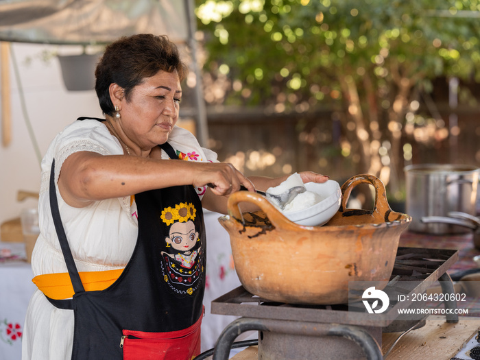 一位土著妇女将食材舀入传统粘土锅的水平视图