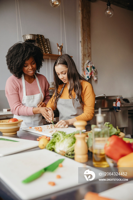 Chef assisting female student in chopping food on cutting board at cooking class