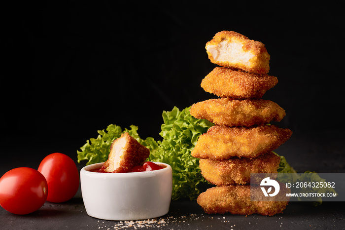 A stack of chicken nuggets and a bowl with ketchup and lettuce on a dark background