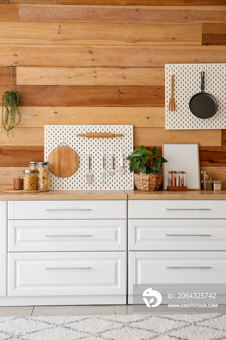 Interior of modern kitchen with white counters, peg boards and wooden wall