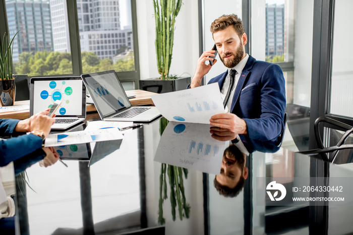 Handsome analytic manager working with paper charts and laptop at the luxury office interior