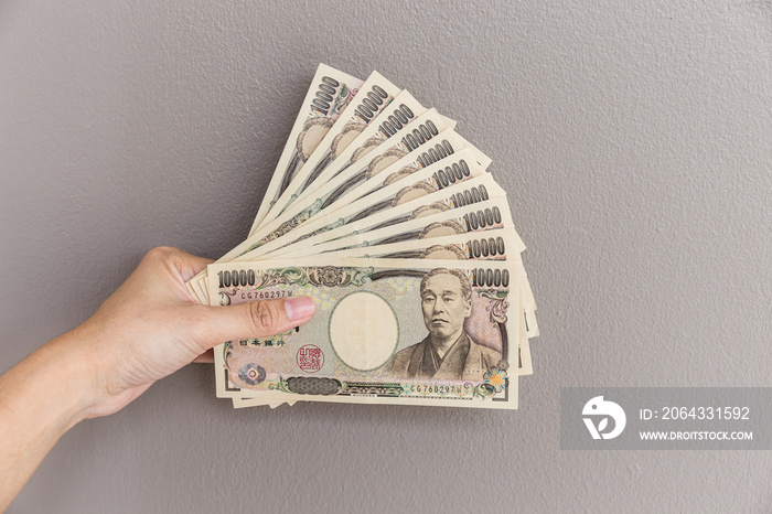 Businesswoman giving money and holding 10,000 japanese yen money in hand on gray wall background, Ja