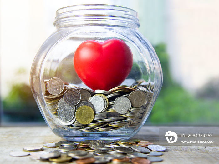 Concept pay attention in saving. Red heart in glass jar with coins.