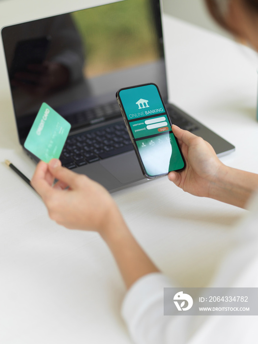 Female hand using online banking application on smartphone and holding credit card