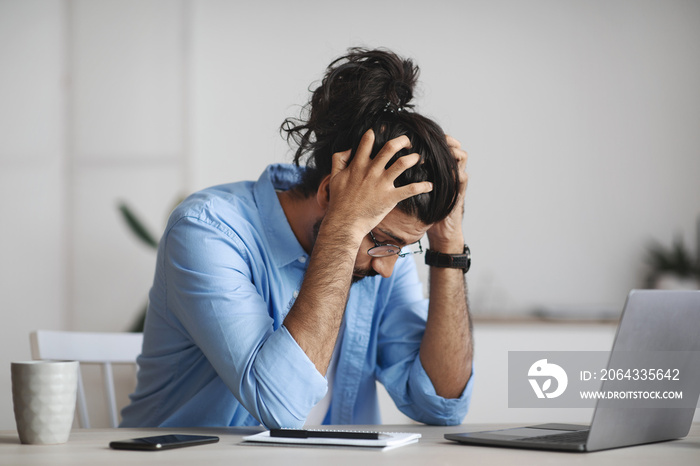 Work Problems. Desperate indian manager sitting at desk in office, suffering from business failure