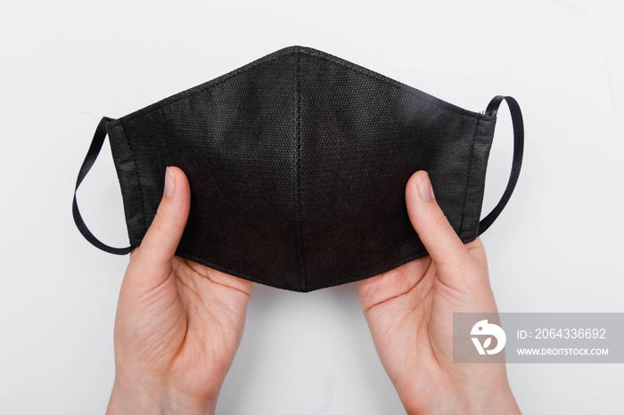 First-person view, close-up of hands holding a handmade black face mask, isolated on white backgroun