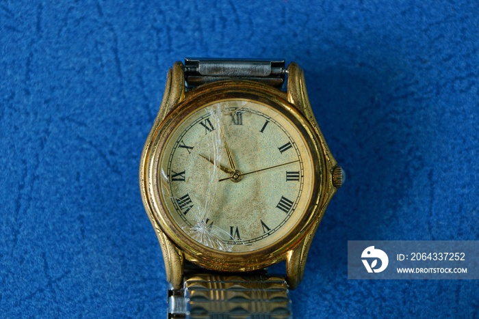 yellow old wrist watch with broken glass on a blue table