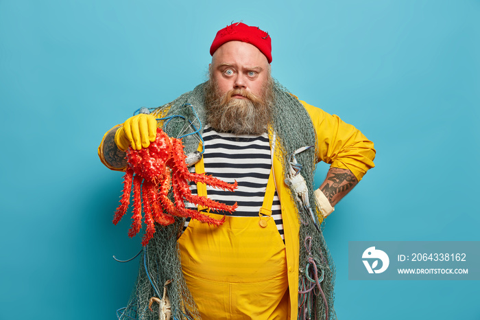 Photo of serious sailor works on ship, holds big octopus, carries fishing net, has sailing expeditio