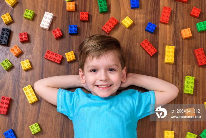 Little caucasian child playing with lots of colorful plastic blocks indoor. Kid boy wearing shirt an