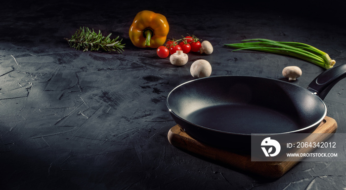 Empty pan on dark table surrounded by vegetarian cuisine ingredients