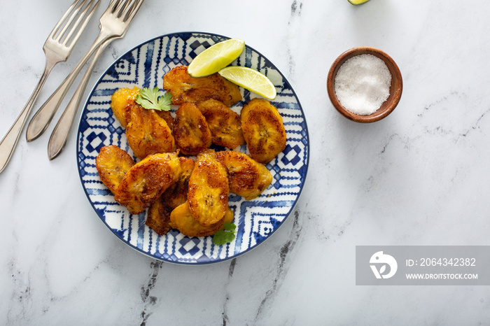 Fried caramelized plantains served with lime wedges and cilantro overhead shot