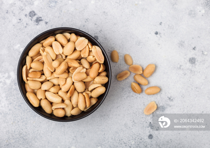 Salted and roasted peanuts classic snack in black bowl on light background.