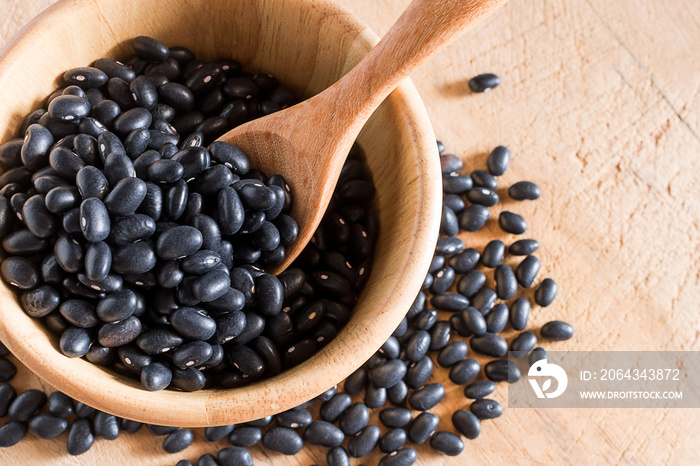 Raw black beans in wooden bowl and spoon on table.