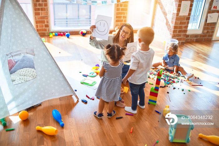 Beautiful psychologist and group of toddlers make therapy using emotions emojis around lots of toys 