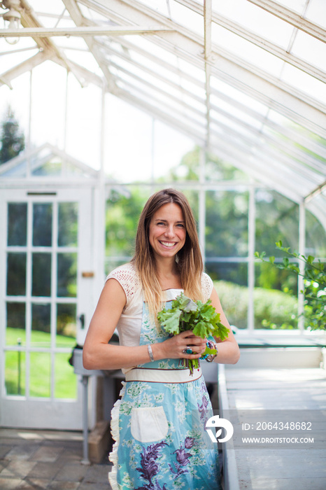 Portrait of woman holding fresh vegetables in greenhouse