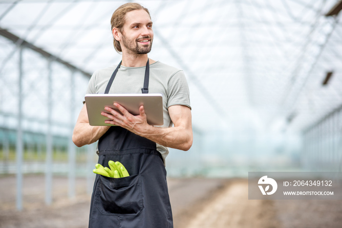 Handsome farmer working with digital tablet standing in the glasshouse with cultivated soil