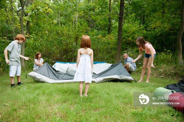 Family folding up tent in forest