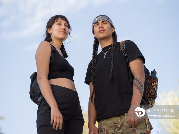 Up view image of Indigenous friends standing close and looking out onto the mountains