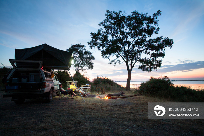 Couple camping by off-road vehicle in forest at dusk