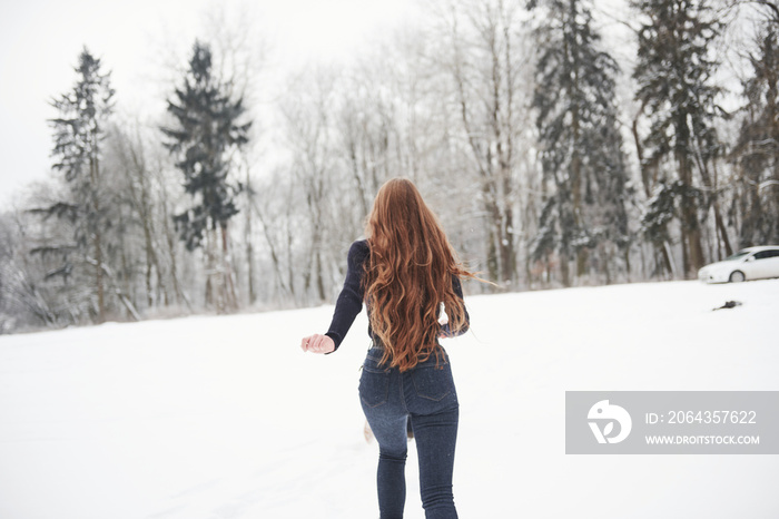 Rear view of girl with long hair runs near the forest to the automobile in wintertime