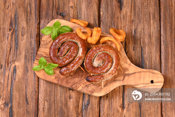 Roasted spicy spiral sausage with basil leaves and fried fries.